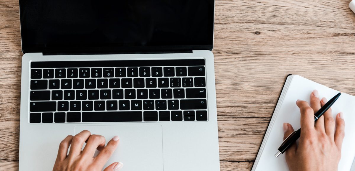 top view of woman holding pen while using laptop with blank screen